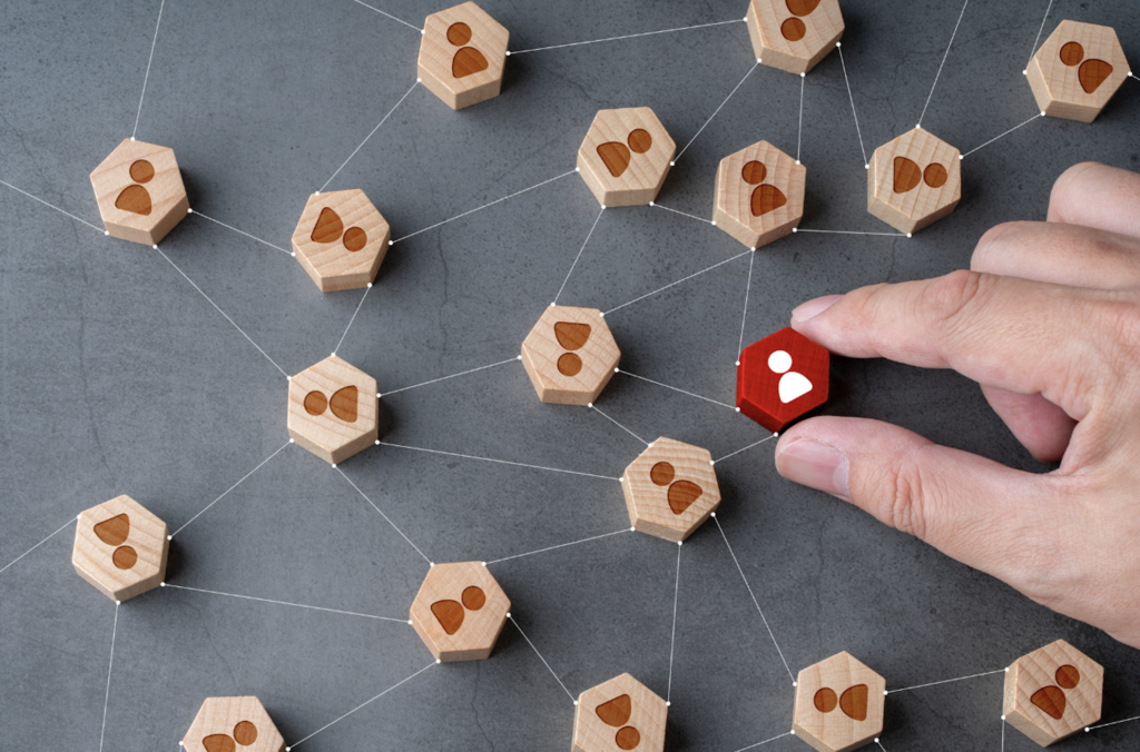 Hand holding red hexagon with white image of person. The hexagon is in a web of other wooden hexagon with human silhouettes