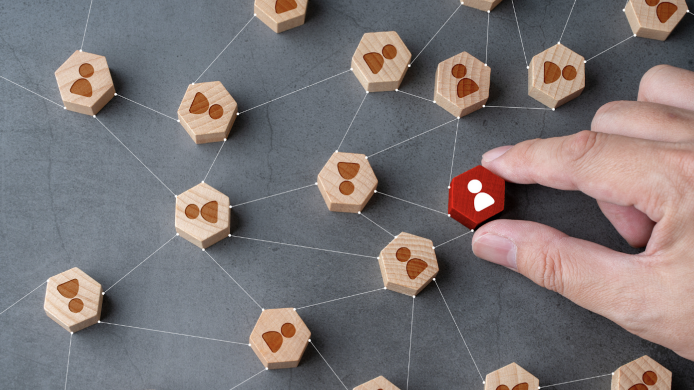 Hand holding red hexagon with white image of person. The hexagon is in a web of other wooden hexagon with human silhouettes